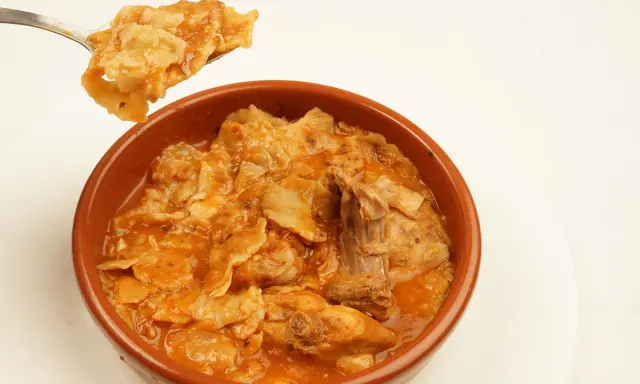 Un plato humeante de comida típica de Albacete, con trozos de carne y pasta en una salsa rojiza.