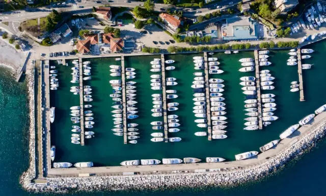 Widok z lotu ptaka na port w Chorwacji, pełen białych jachtów i łodzi zacumowanych w turkusowej wodzie.