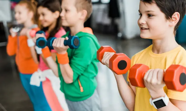 Dzieci ćwiczą z hantlami podczas zajęć si. Uśmiechnięci mali sportowcy budują siłę.