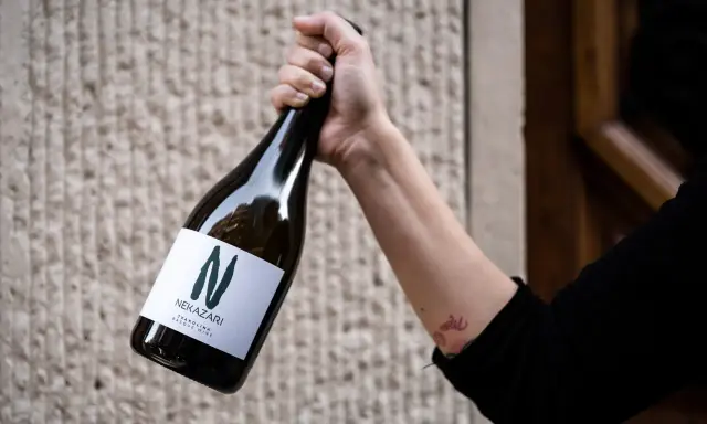 Mano sujeta botella de txakoli tinto Nekazari, con etiqueta blanca y letra "N" verde.