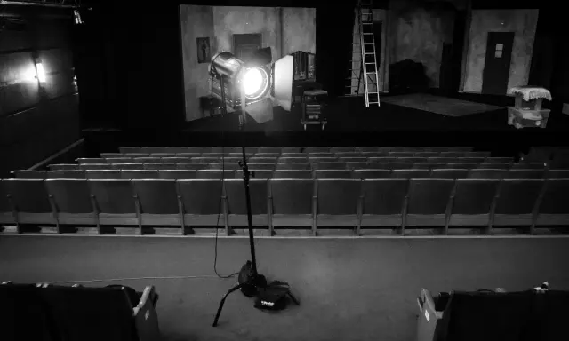 Teatr w czerni i bieli. Na scenie reflektor fresnel oświetla dekoracje, a przed nią puste rzędy siedzeń.