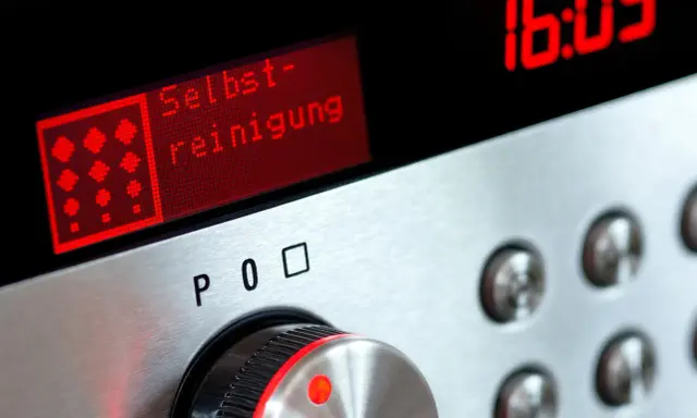Bedienfeld eines Ofens mit rotem Display, das "Selbst-reinigung" anzeigt. Daneben die Uhrzeit 16:05.