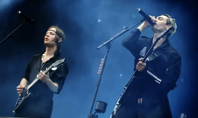 Gustaf Norén sjunger och spelar gitarr med Mando Diao på scenen, omgiven av rök och blått ljus.