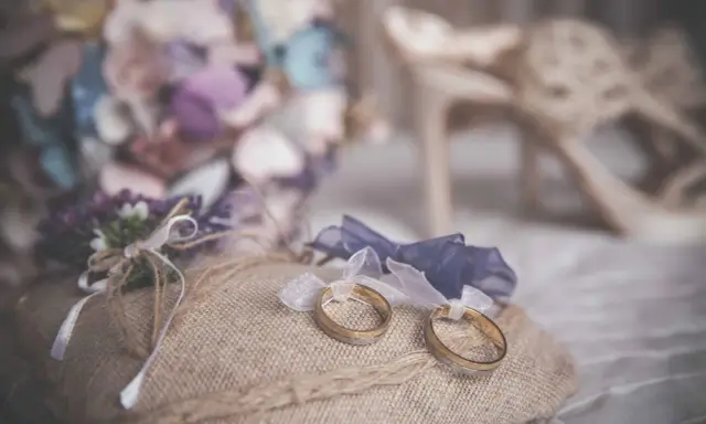 Anillos de boda sobre cojín rústico, ideas para decorar la habitación donde se viste la novia con flores y zapatos elegantes.