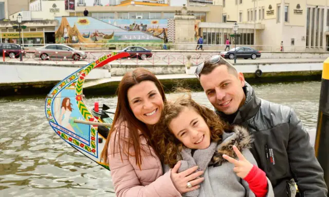 Familia feliz disfrutando de un paseo en góndola en Aveiro con niños. La niña hace el signo de la paz.