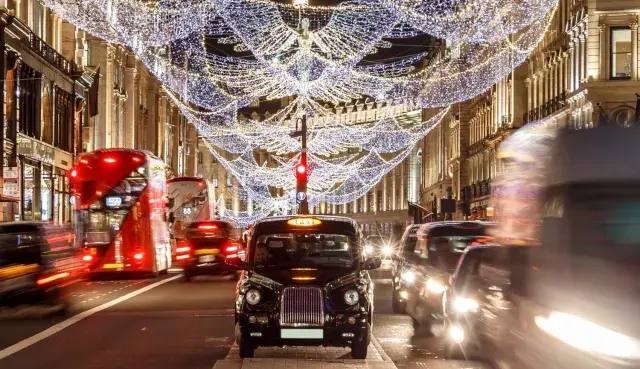 Julbelysning i London i december. Röda dubbeldäckare och taxibilar susar förbi på en livlig gata.