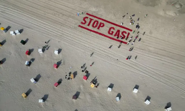 Menschen bilden auf einem Strand "STOP GAS!" als Zeichen für Deutschland klimaneutral. Viele Strandkörbe sind zu sehen.