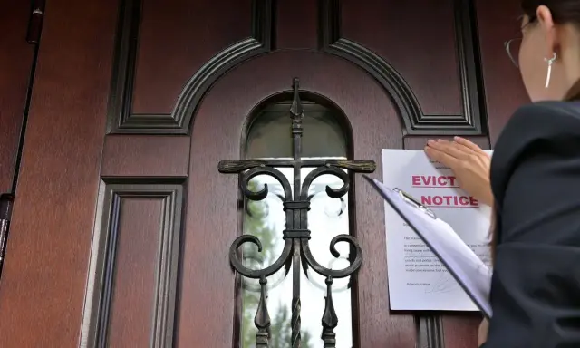 Mujer coloca un aviso de desalojo en una puerta de madera. Proceso para como echar a un inquilino sin contrato.