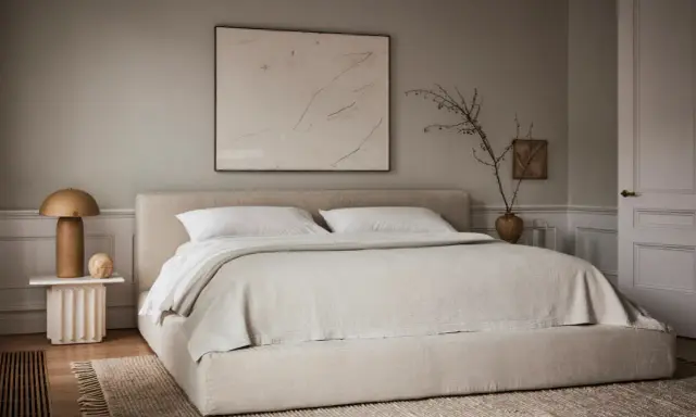 Une chambre beige apaisante avec un lit bas, une table de chevet sculpturale et une œuvre d'art abstraite.