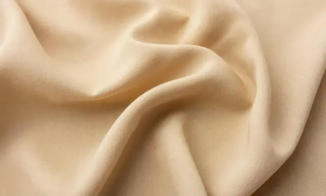 A close-up of draped beige viscose fabric. It feels smooth and cool, like silk, with a subtle sheen.