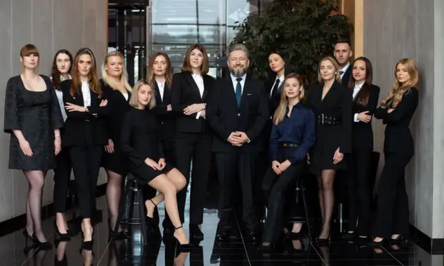 Grupa prawników i radców prawnych w eleganckich strojach stoi w nowoczesnym wnętrzu.