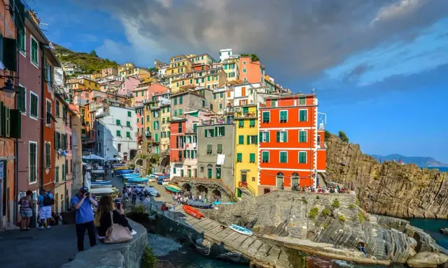 Bunte Häuserfronten der Cinque Terre Orte schmiegen sich an steile Felsen. Boote liegen im türkisfarbenen Wasser.