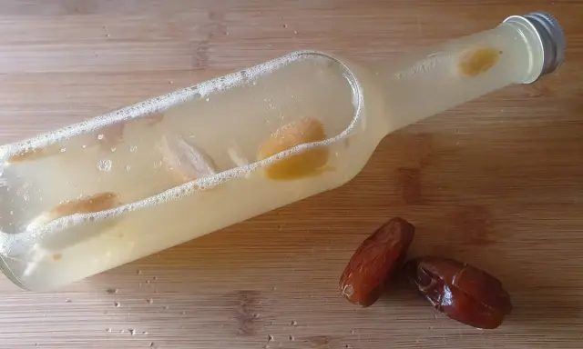 Flasche mit Flüssigkeit und Fruchtstücken, bereit zum Hefe selber machen. Daneben liegen zwei Datteln.