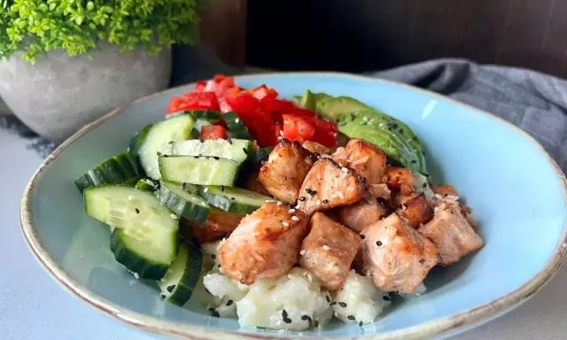 Pyszny bowl z kawałkami pieczonego lososia, świeżym ogórkiem, pomidorem i awokado na ryżu.