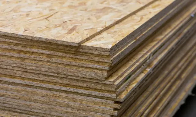 Stos płyt OSB, idealnych jako podkład pod pokrycie dachowe. Zastanawiasz się, czym pokryć dach z płyty OSB? Oto materiał, który Ci w tym pomoże.