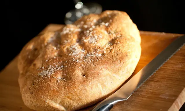 Focaccia rustica con sale grosso e rosmarino, pronta per essere tagliata. Un invito a gustare, come il pan per focaccia significato.