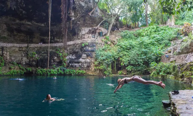 Una ragazza si tuffa nel **cenote Zaci**, un'oasi naturale con acque cristalline e vegetazione lussureggiante.