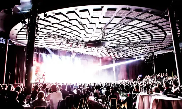 Publik njuter av en konsert på Rondo Liseberg. Scenen badar i ljus, taket är dekorerat med akustikpaneler.