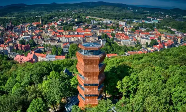 Nowoczesna wieża widokowa w otoczeniu zieleni, z panoramą miasta i Gór Wałbrzyskich w tle.