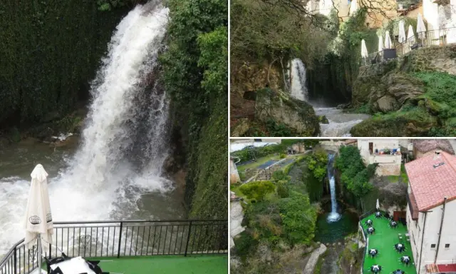 Cascada y terrazas con mesas junto a piscinas naturales en Burgos. Paisaje verde con casas rurales y agua cayendo.