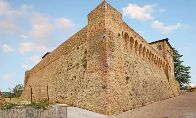 Antica fortezza nella valle del Rubicone, con mura in pietra e mattoni, torri e un loggiato ad archi.