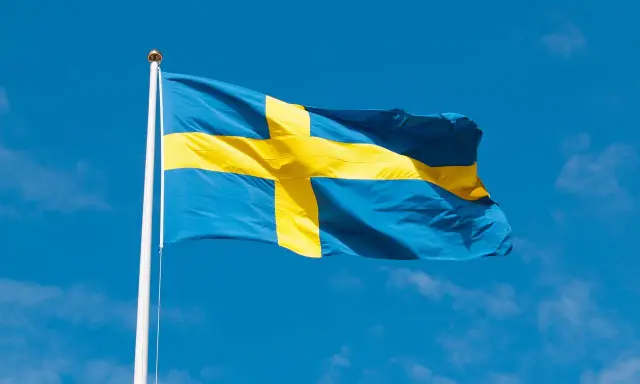 Svenska flaggan vajar i blå himmel. Dess korsdesign har en lång svenska flaggan historia, symboliserande nationens arv.