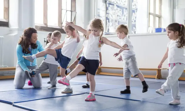 Niños aprendiendo movimientos de **deportes para niños** con una maestra en un gimnasio.