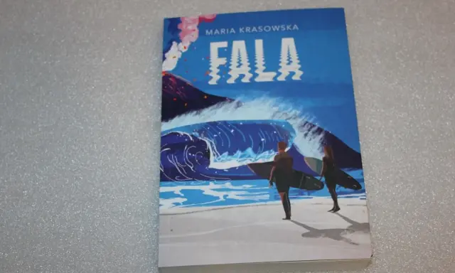 Okładka książki "Fala" Marii Krasowskiej. Dwie postacie z deskami surfingowymi stoją na plaży, patrząc na ogromną falę i wulkan.