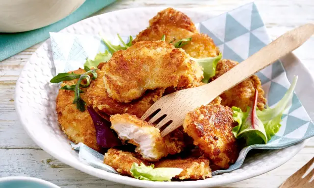 Knusprige Hähnchen-Nuggets, perfekt im Butterschmalz gebraten, auf einem Bett aus Salat. Ein Holzgabel liegt bereit.