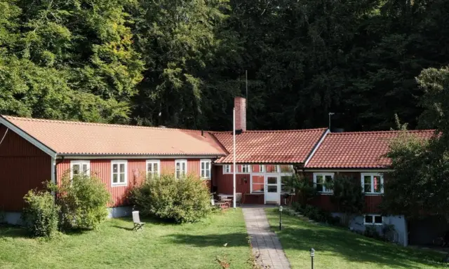Stocklycke vandrarhem, ett rött hus med tegeltak, omgivet av grönskande träd och en välskött gräsmatta.