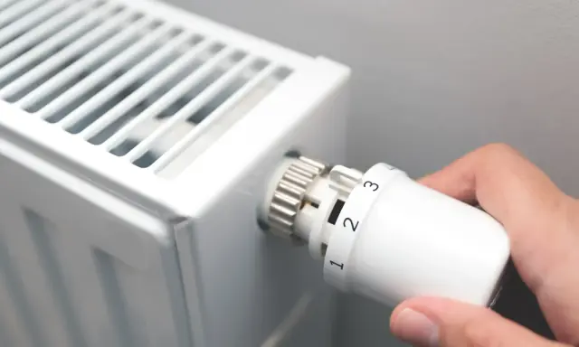 Dłoń kręci termostatem grzejnika, ustawiając temperaturę. To znak, że zbliża się czas, kiedy zaczyna się sezon grzewczy.