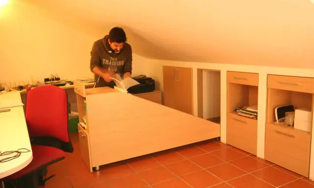 Uomo in mansarda con idee sottotetto molto basso: scrivania angolare, armadi a muro e sedia rossa.