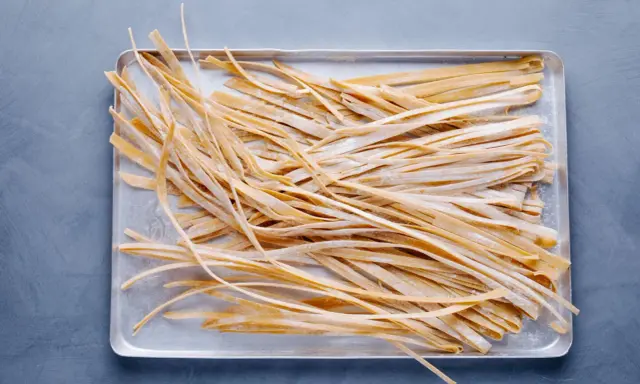 Frische, selbstgemachte Tagliatelle liegen auf einem Blech, bereit zum Kochen. Das Ergebnis von Tagliatelle selber machen.