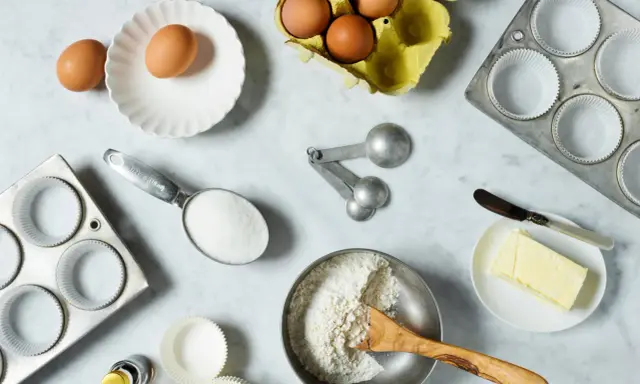 Backzutaten: Eier, Mehl, Zucker, Butter, Muffinförmchen und Messlöffel im amerikanischen Maßsystem.