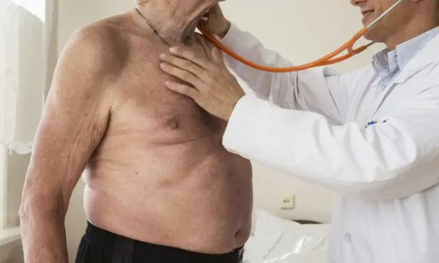 Lekarz osłuchuje klatkę piersiową starszego mężczyzny stetoskopem.
