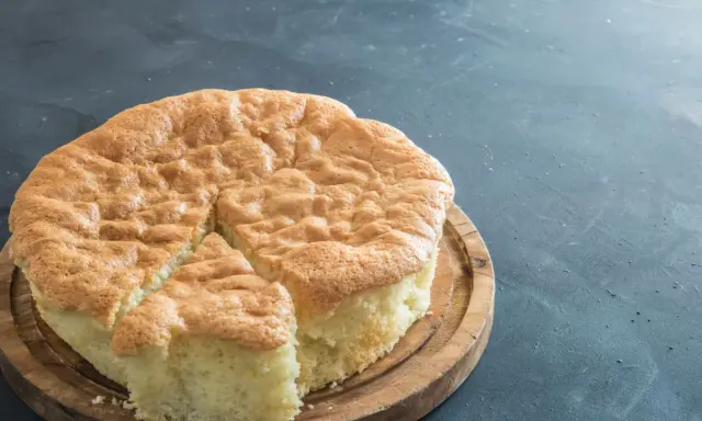 Un gâteau raté, un peu affaissé, sur une planche en bois. Sa texture est spongieuse et sa croûte dorée.