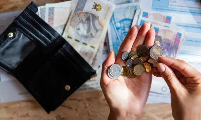 Otwarty portfel, polskie banknoty i monety w dłoni na tle dokumentów.