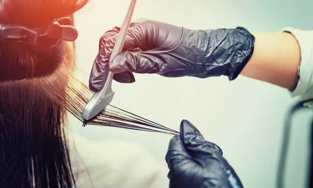 Mani guantate applicano tinta ai capelli. Scopri quanto dura una tinta dal parrucchiere per un colore impeccabile.