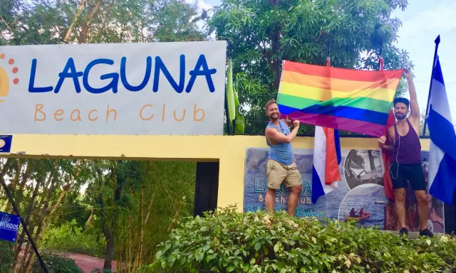 Two men proudly hold a rainbow flag at Laguna Beach Club, celebrating gay pride in Guatemala.
