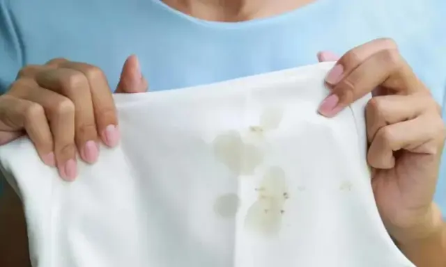 Manos sostienen tela blanca con manchas de grasa. Aprende como quitar la grasa de la ropa fácilmente.