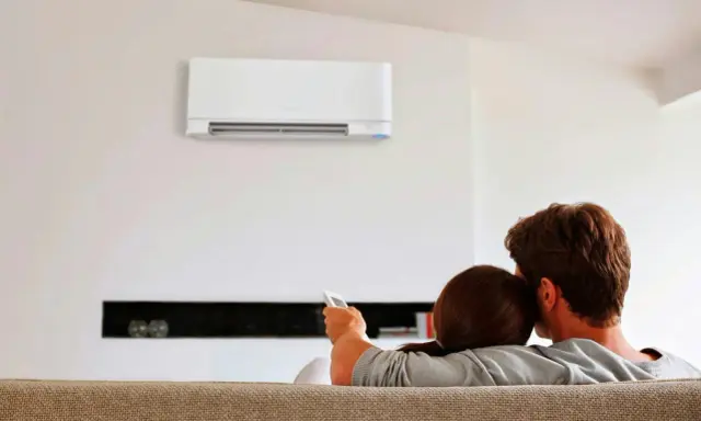 Pareja relajada en el sofá, disfrutando del confort que ofrece un **split aire acondicionado** en la pared.
