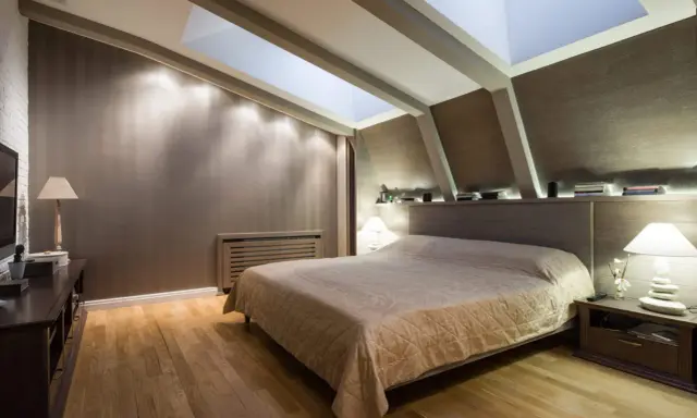 Chambre douillette avec un lit confortable sous une **tête de lit sous pente** et un puits de lumière illuminant la pièce.