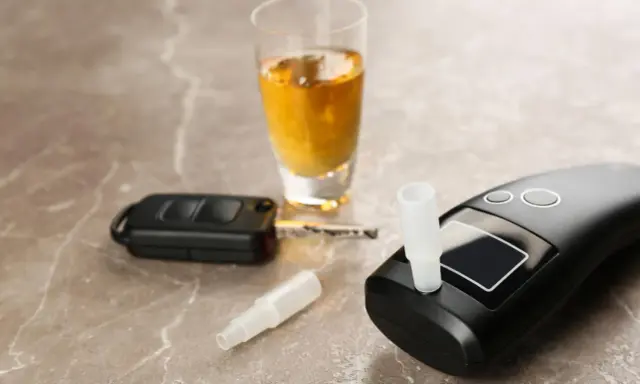 Alkomat, kluczyki samochodowe i kieliszek z alkoholem na marmurowym blacie.