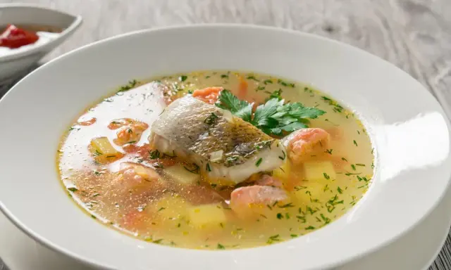Aromatyczna zupa rybna przepis: delikatny filet rybny, kawałki łososia, ziemniaki i marchewka w bulionie, ozdobiona natką pietruszki.