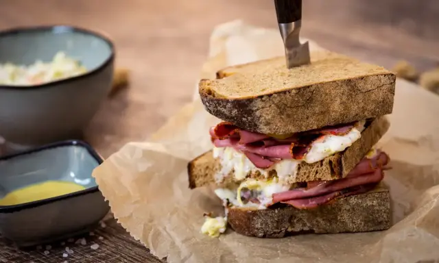 Ein üppiges Pastrami-Sandwich mit Röstbrot, serviert mit Beilagen wie Krautsalat und Senf.