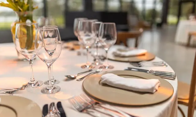Une table élégamment dressée pour un repas, avec la position des verres à la française. Des assiettes, serviettes et couverts sont prêts.