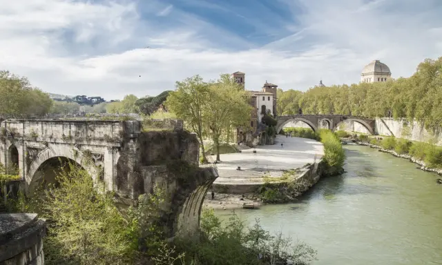 Un ponte rotto, con archi antichi e vegetazione rigogliosa, domina un fiume serpeggiante a Roma.