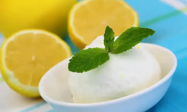 Crème glacée citron rafraîchissante, garnie de menthe fraîche, avec des citrons coupés en arrière-plan.