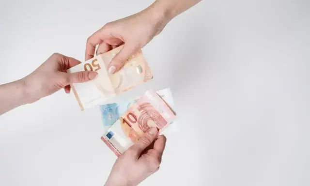 Dwie ręce przekazują sobie banknoty euro. To waluta Słowenii, używana do codziennych zakupów.