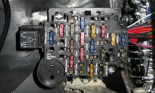 Caja de fusibles de coche con varios fusibles de colores y etiquetas. Aprende cómo quitar un fusible del coche para reparaciones.